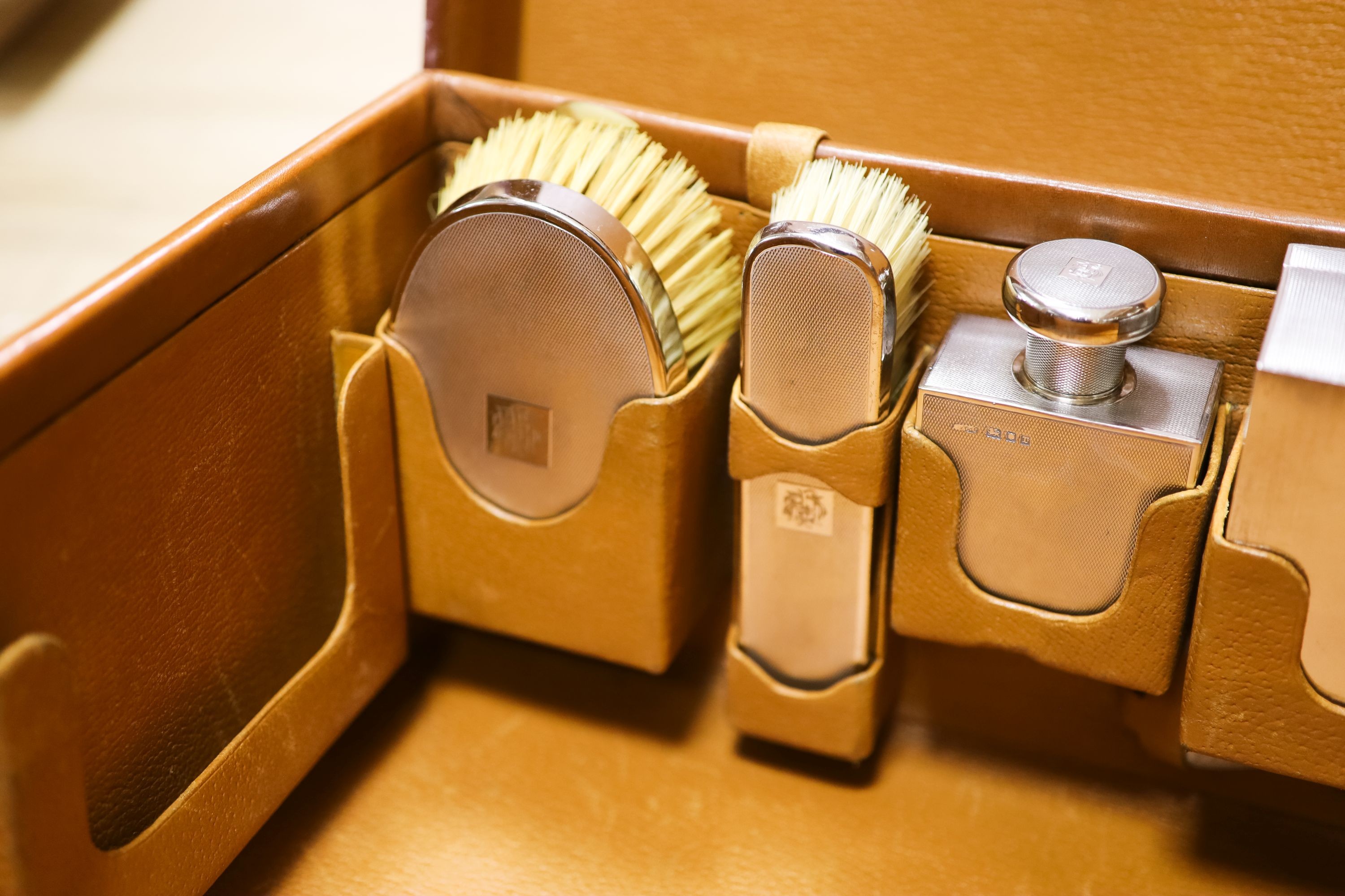 A 1930's Harrods pigskin travelling toilet case with seven engine turned silver fittings, including brushes, cigarette box and two scent bottles, F & Co Ltd, London, 1933, case 66.5cm.